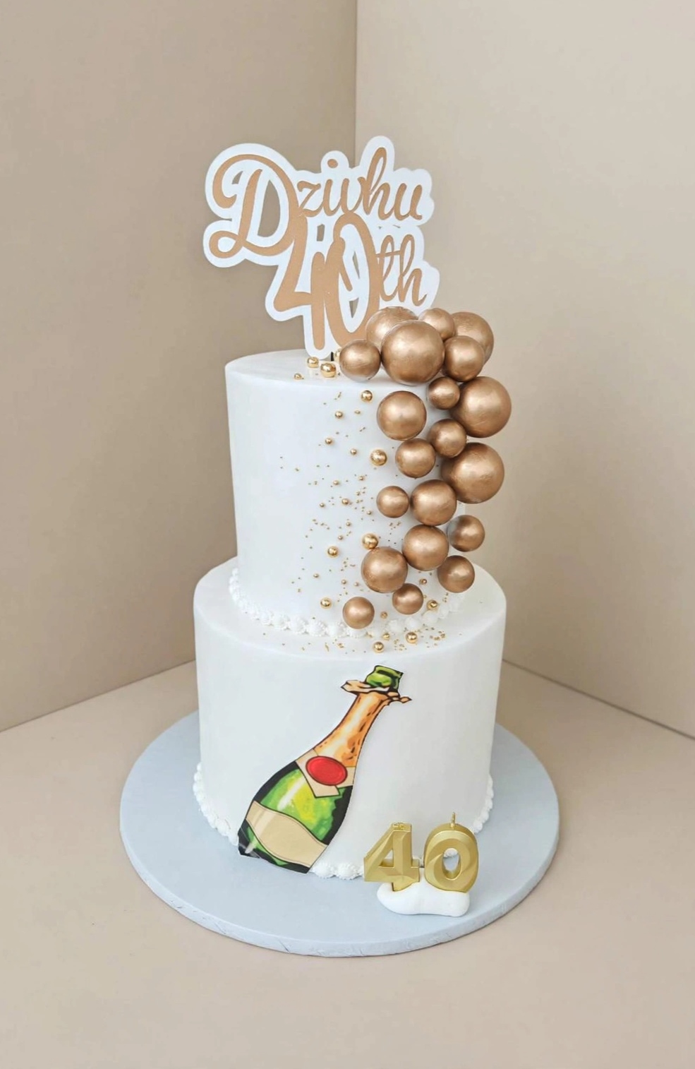 Two-tier white and gold 40th birthday cake with champagne bottle