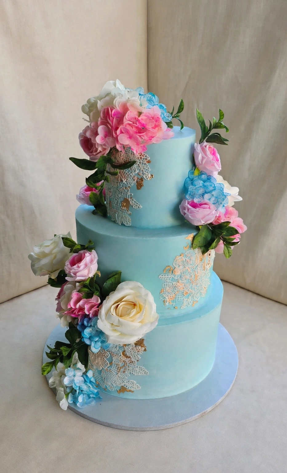 Three-tier soft blue wedding cake with florals and lace