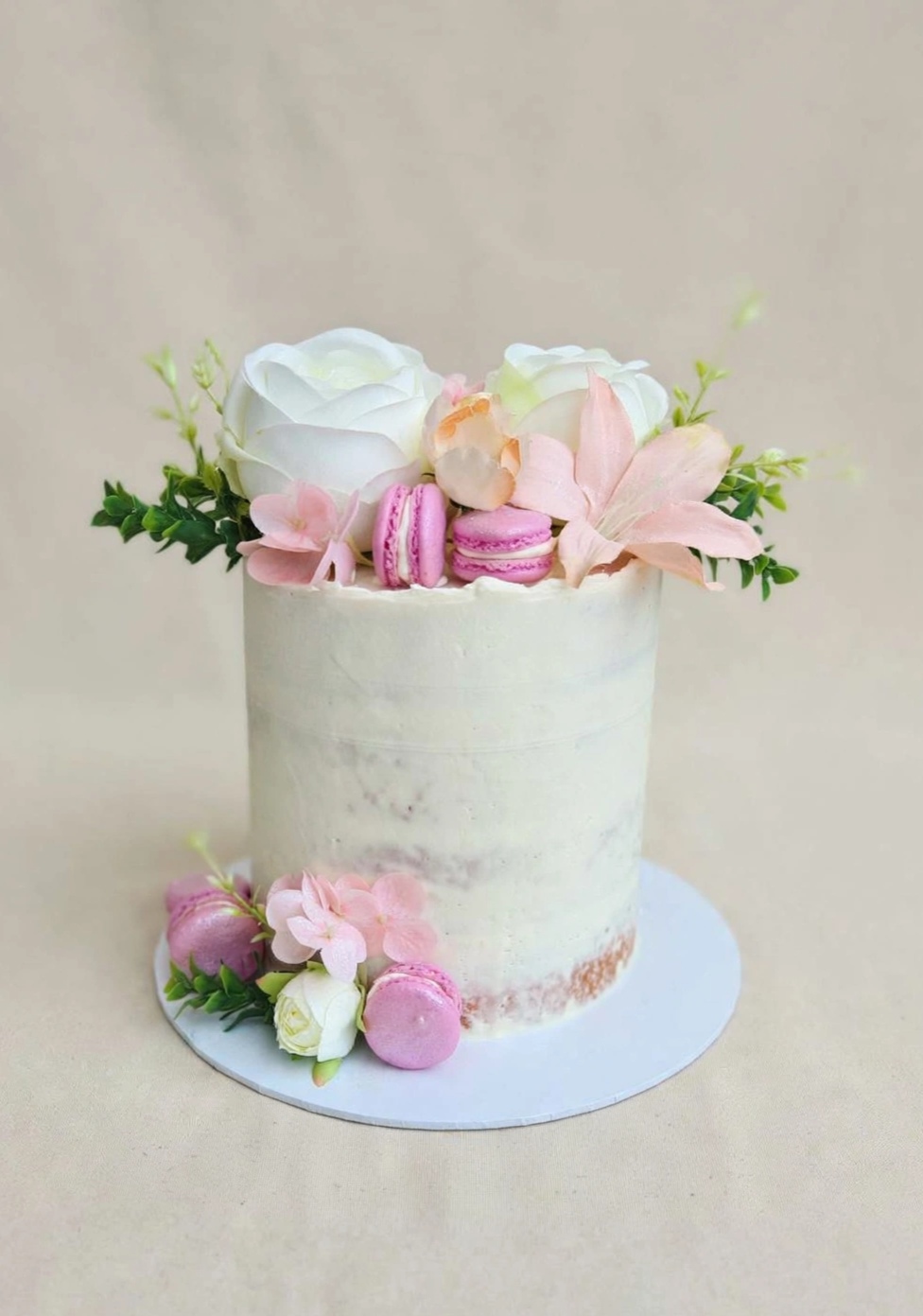 Semi-naked buttercream cake topped with roses, lilies and macarons