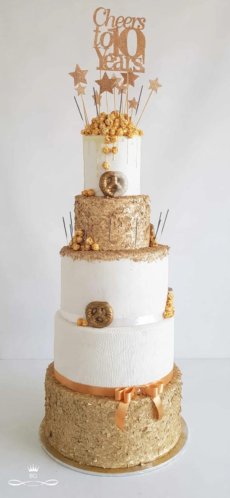 Five-tier white and gold 10th birthday cake with caramel popcorn and a Cheers to 10 Years topper